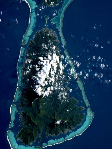 Raiatea, French Polynesia, photographed from the International Space Station: a high volcanic island ringed by its barrier reef and lagoon. Image: ESA/NASA – S. Adenot.